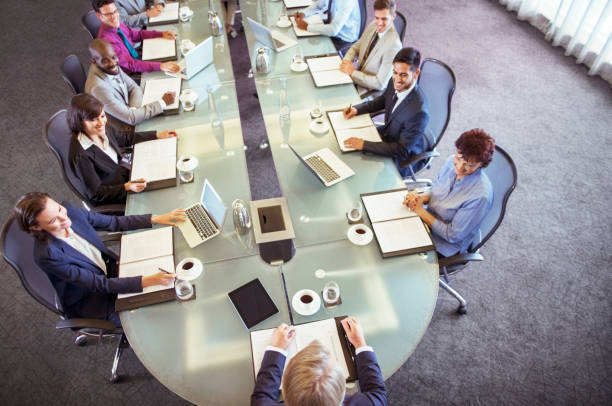 gruppe von geschäftsleuten, die am konferenztisch sitzen und den vorsitzenden betrachten - office water business meeting stock-fotos und bilder