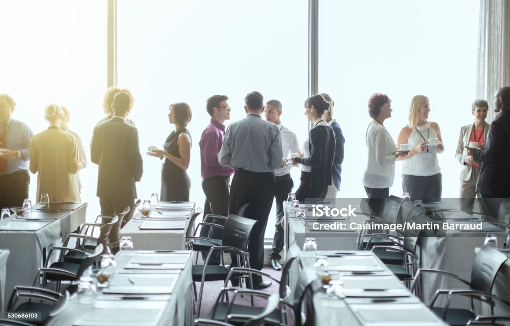 Group of people standing by windows of conference room, socializing during coffee break  Meeting Stock Photo
