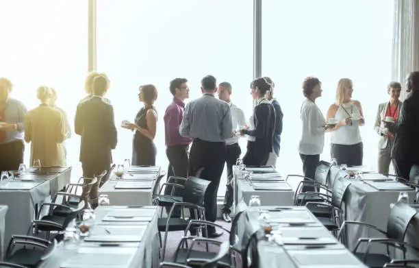 Photo of Group of people standing by windows of conference room, socializing during coffee break