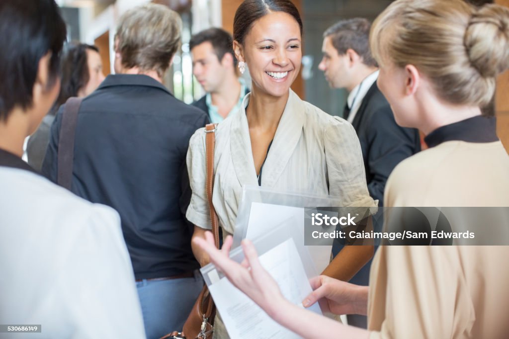Portrait of two smiling women holding files and talking, standing in crowded lobby  Connection Stock Photo