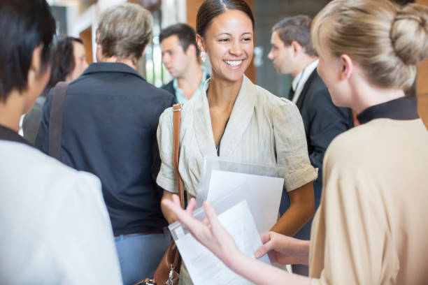 Portrait of two smiling women holding files and talking, standing in crowded lobby  business conference stock pictures, royalty-free photos & images