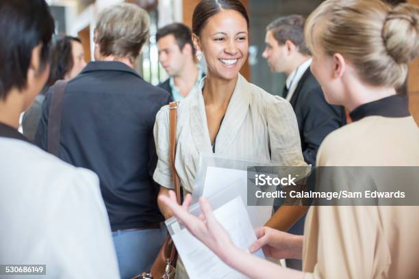 Portrait Of Two Smiling Women Holding Files And Talking Standing In Crowded Lobby Stock Photo - Download Image Now