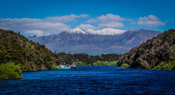 Lake Manapouri, New Zealand, blue water, high mountains, snow, forest, ships, blue sky