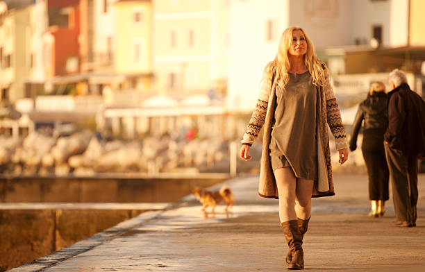 Attractive Mature Woman In Woolen Clothings Walking in Piran, Slovenia Attractive mature woman with long blond hair in woolen clothings in nature colors walking at seaside on a sunny winter day. Piran, Slovenia, Europe. older women short skirts stock pictures, royalty-free photos & images
