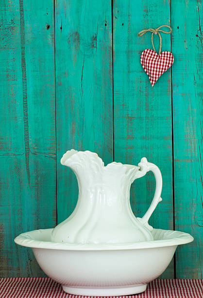 Antique white water pitcher and basin on gingham tablecloth by rustic teal blue wooden background with red checkered heart