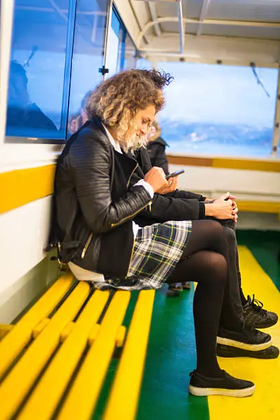 Young couple(students) on a ferryboat traveling over Bosporus from School towards their home. They are having fun with their smart phone. Cold autumnal evening. Nikon D800, full frame, XXX. Very soft focus.