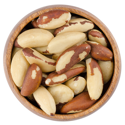 Raw brazil nuts in a wooden bowl from above, isolated on white background.