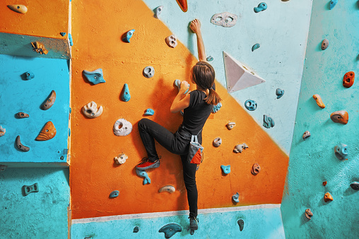 Woman climbing up on wall at bouldering gym. Female climber training, hanging on bouldering climbing wall. Active lifestyle and extreme sport concept.