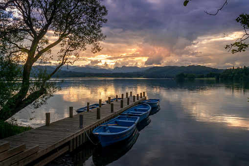 Rowing boats moored alongside a wooden jetty. Vivid sunset and cloudscape backdrop