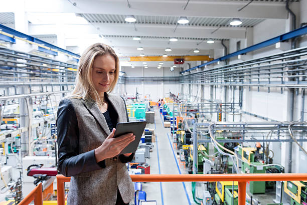 Female quality inspector using tablet Horizontal color image of blond business female worker standing on balcony on top of large factory, holding digital tablet and examining the production online. Focus on attractive businesswoman, futuristic machines in background polymer photos stock pictures, royalty-free photos & images