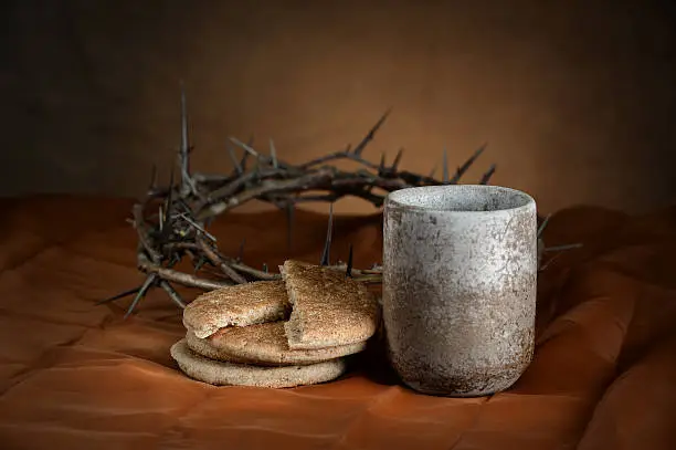 Communion cup and bread with crown of thorns in background