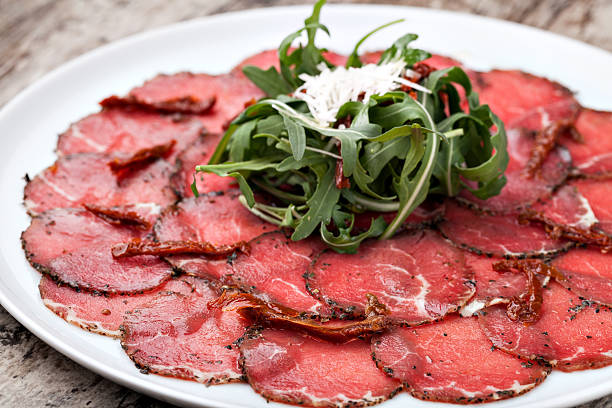 white dish with carpaccio of beef on arugula