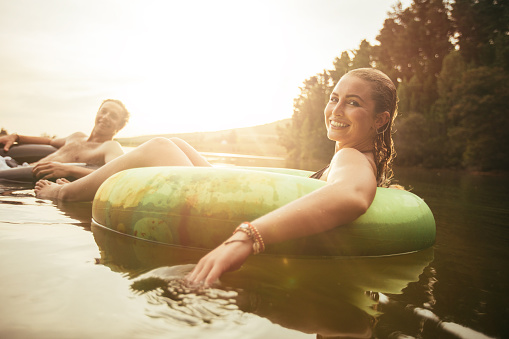 Portrait of happy young woman in lake on inflatable ring with her boyfriends in background. Young couple relaxing in water on a summer day.