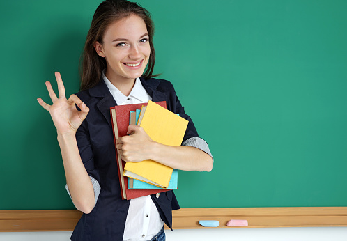 Happy smiling student showing okay gesture. Photo of teen near blackboard, education concept