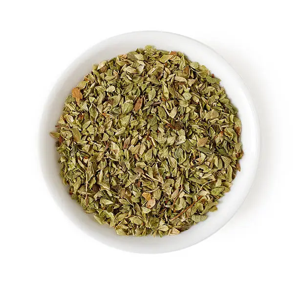 Bowl of dried oregano leaves isolated on white background, top view