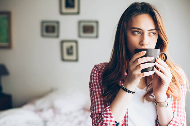 mujer joven de pie en dormitorio y bebiendo café - café bebida fotos fotografías e imágenes de stock