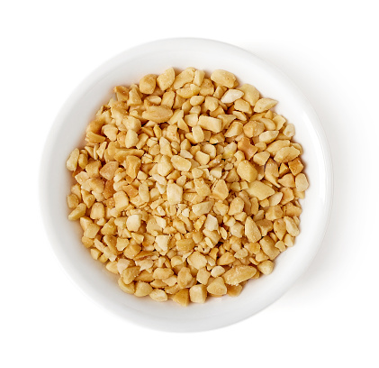 Bowl of roasted crushed peanuts isolated on white background, top view