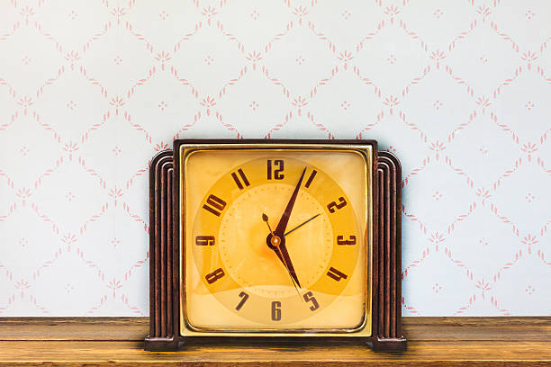istock Vintage table clock in front of retro wallpaper 530750280
