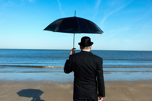Englishman with bowler hat and umbrella  on the beach overlooking the sea and towards Europe.