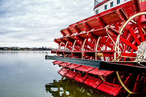 Red and white paddlewheeler docked on the rivers edge.