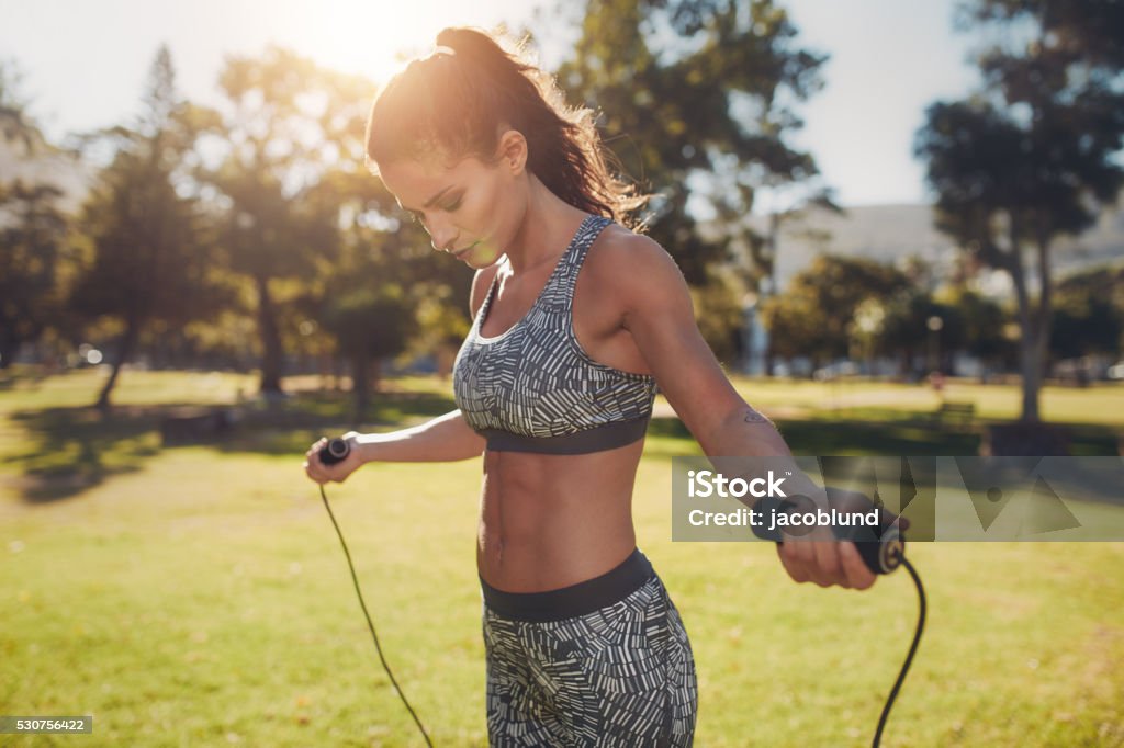 Fit young woman with jump rope in a park Portrait of fit young woman with jump rope in a park. Fitness female doing skipping workout outdoors on a sunny day. Jumping Rope Stock Photo