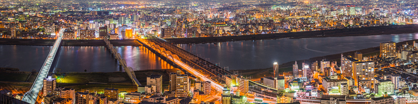 The bright lights of Osaka's crowded cityscape joined by the highway and rail bridges across the Yodo River, Japan. ProPhoto RGB profile for maximum color fidelity and gamut.