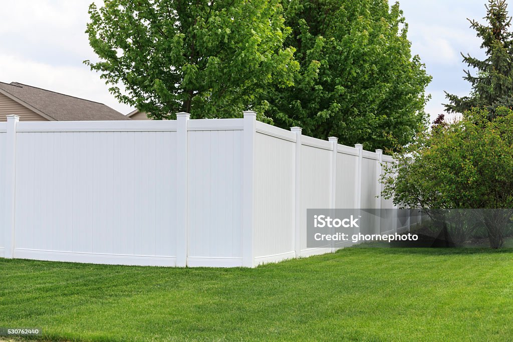 White vinyl fence A white vinyl fence running across a yard on spring day with blue sky and trees in the background Fence Stock Photo