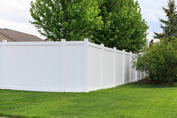 White vinyl fence A white vinyl fence running across a yard on spring day with blue sky and trees in the background fence stock pictures, royalty-free photos & images