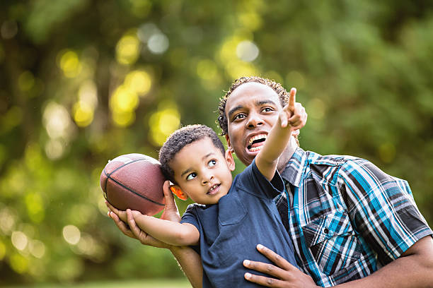 African American Father and Young Son outdoors playing football stock photo