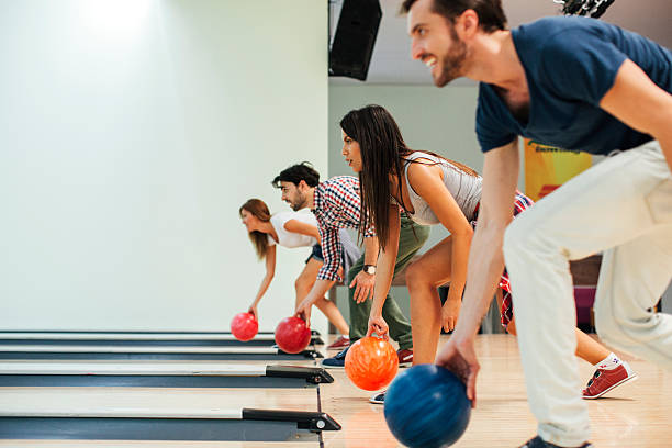 Cheerful Friends Bowling Together. Group of happy friends having fun, bowling together. Side view of them bowling. bowling alley stock pictures, royalty-free photos & images