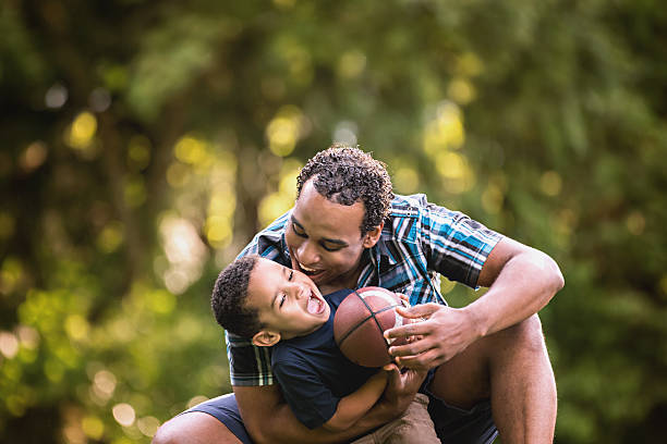 afroamerikanischen vater und sohn fußball zu spielen im freien jungen - child american football football sport stock-fotos und bilder