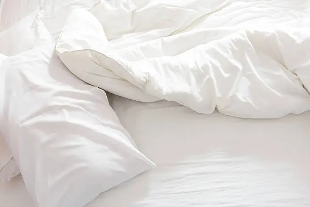 Top view of an unmade bed with crumpled bed sheet, a blanket and pillows after waking up in the morning.