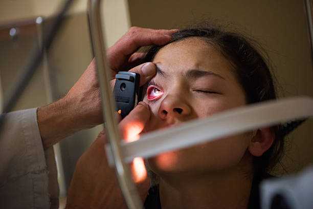 Doctor Examines Patient's Eye in Dark Room with Handheld Lens stock photo