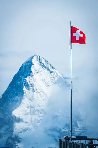 The vibrant red and white Swiss flag flying high on the Schilthorn overlooking the iconic summit and north face of the Eiger (3970m) deep in the Alpine mountains of Switzerland. ProPhoto RGB profile for maximum color fidelity and gamut.