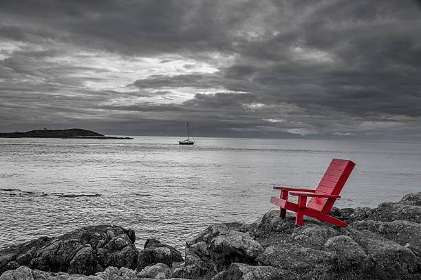 Sea side contrast Red chair on ocean side rocks contrasts with the stormy black and white background. vancouver island photos stock pictures, royalty-free photos & images