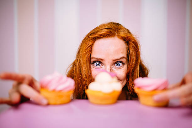 Young red head woman really wants to eat pink cupcakes