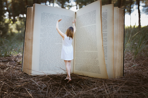 Magic big book standing young woman on forest.