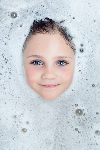littel blond girl looks through bath foam 6 year old girl blond smiling girl with blue eyes looks through white bath foam. girls bath stock pictures, royalty-free photos & images