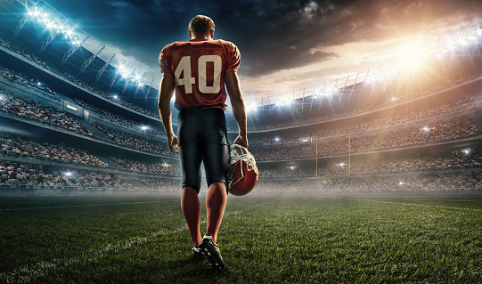 Professional American football player standing on a sport stadium with spotlight. Player is wearing unbranded football cloths. Professional American football player standing on a sport stadium with spotlight. Player is wearing unbranded football cloths. 