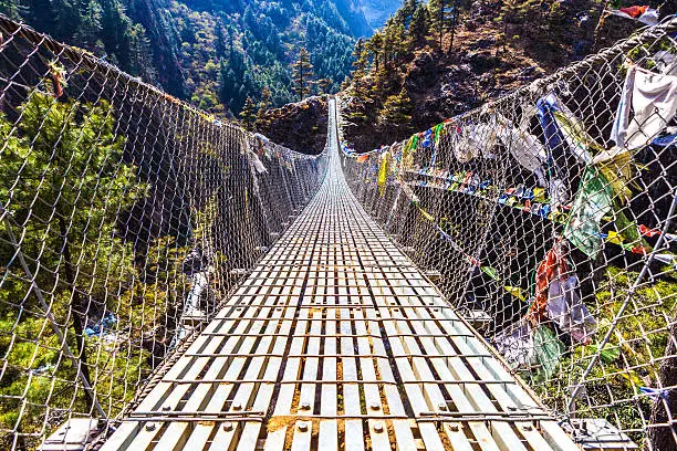 Low angle view of the Dughla Waterfall suspension footbridge with prayer flags located in the Lobuche Valley, Nepal.