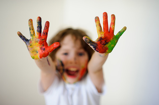 The boy himself dirty in the paint and show his dirty hands ti the camera.  Child face and hands in the paint. Child has fun by painting and drawing. Children's creativity. Art for baby.