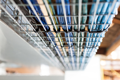 A close up photo of organized wiring inside a home. Wiring is organized by color and grouped together. A metal caging protects the wires.