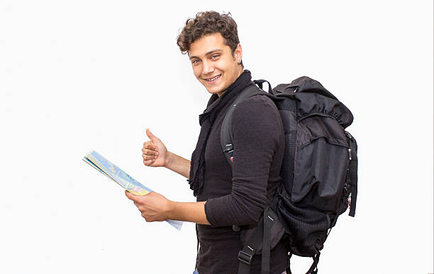 Portrait of a smiling backpacker young man over white background. Happy teenage boy looking at camera with positive, smiling facial expression isolated on white. Smiling boy wearing a black backpack and keeping a map. Studio shot. Horizontal composition. Image developed from RAW format.