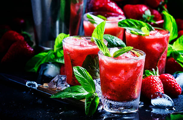 Traditional Brazilian alcoholic cocktail, strawberry caipirinha Traditional Brazilian alcoholic cocktail, strawberry caipirinha with syrup, lime, mint, strawberries and crushed ice, black background, selective focus strawberry crush stock pictures, royalty-free photos & images