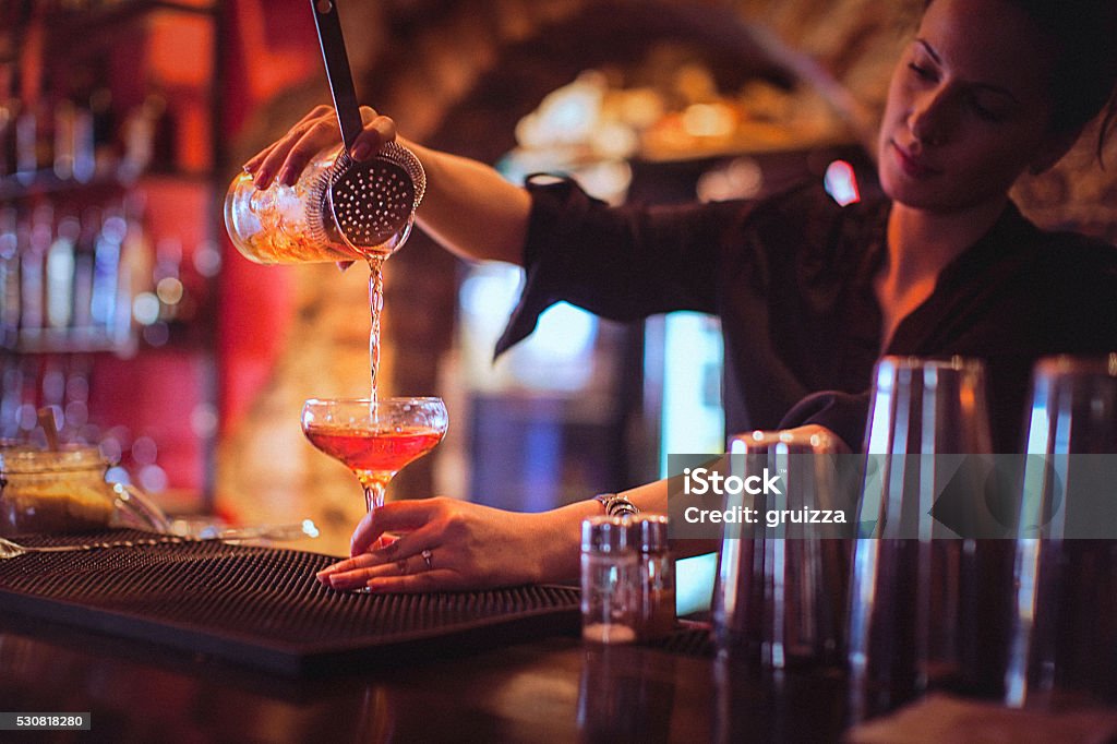 Young female bartender pouring cocktails in a cocktail bar Close-up of a young female bartender pouring cocktail in a nightlife cocktail bar. Selective focus. Focus on foreground. Bar - Drink Establishment Stock Photo