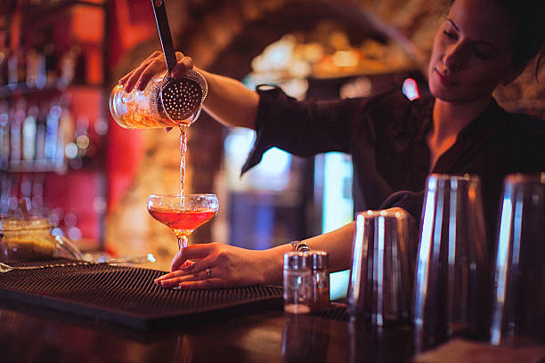 Young female bartender pouring cocktails in a cocktail bar Close-up of a young female bartender pouring cocktail in a nightlife cocktail bar. Selective focus. Focus on foreground. bartender photos stock pictures, royalty-free photos & images