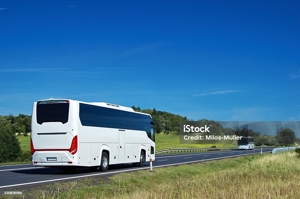 White buses driving on asphalt road in a rural landscape White buses driving on asphalt road in a rural landscape. Sunny summer day with blue skies. Coach Bus Stock Photo