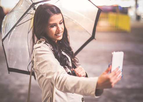 Portrait of young woman taking selfie in the rain with  umbrella