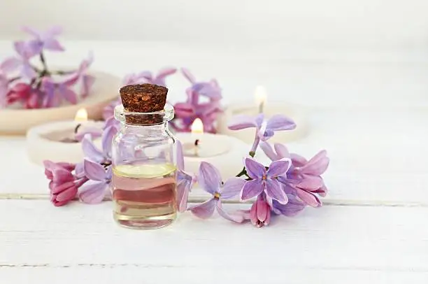 Essential oil in bottle, lilac flowers, tea-candles. Soft focus.