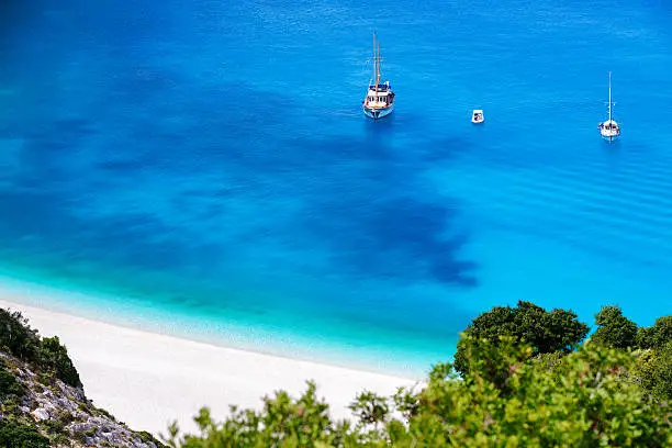 The most famous beach on Kefalonia (Cephalonia), Myrtos. Crystal clear water, some people on the beach and three nautical vessels in the sea. View from above.